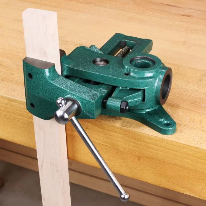 Green woodworking drill press vise holding wood on a workbench