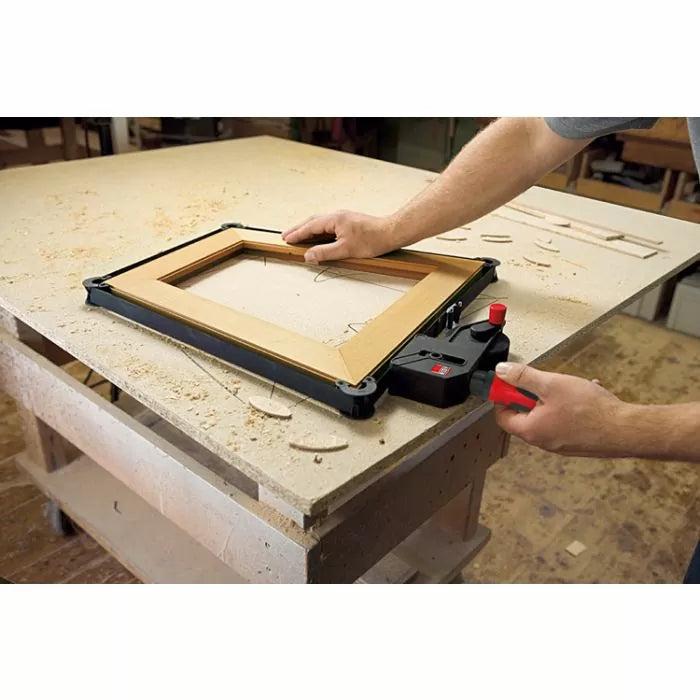 Woodworker using a frame clamping tool on a workbench for precise miter joints