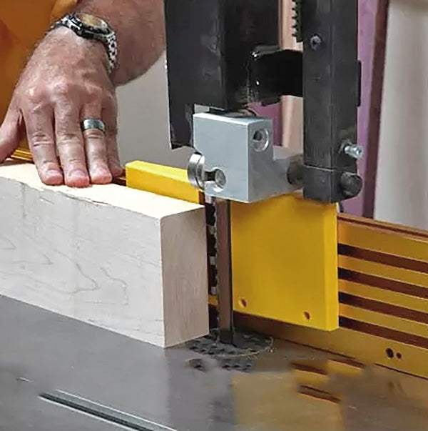 Woodworker using bandsaw with yellow fence to cut thick wooden board