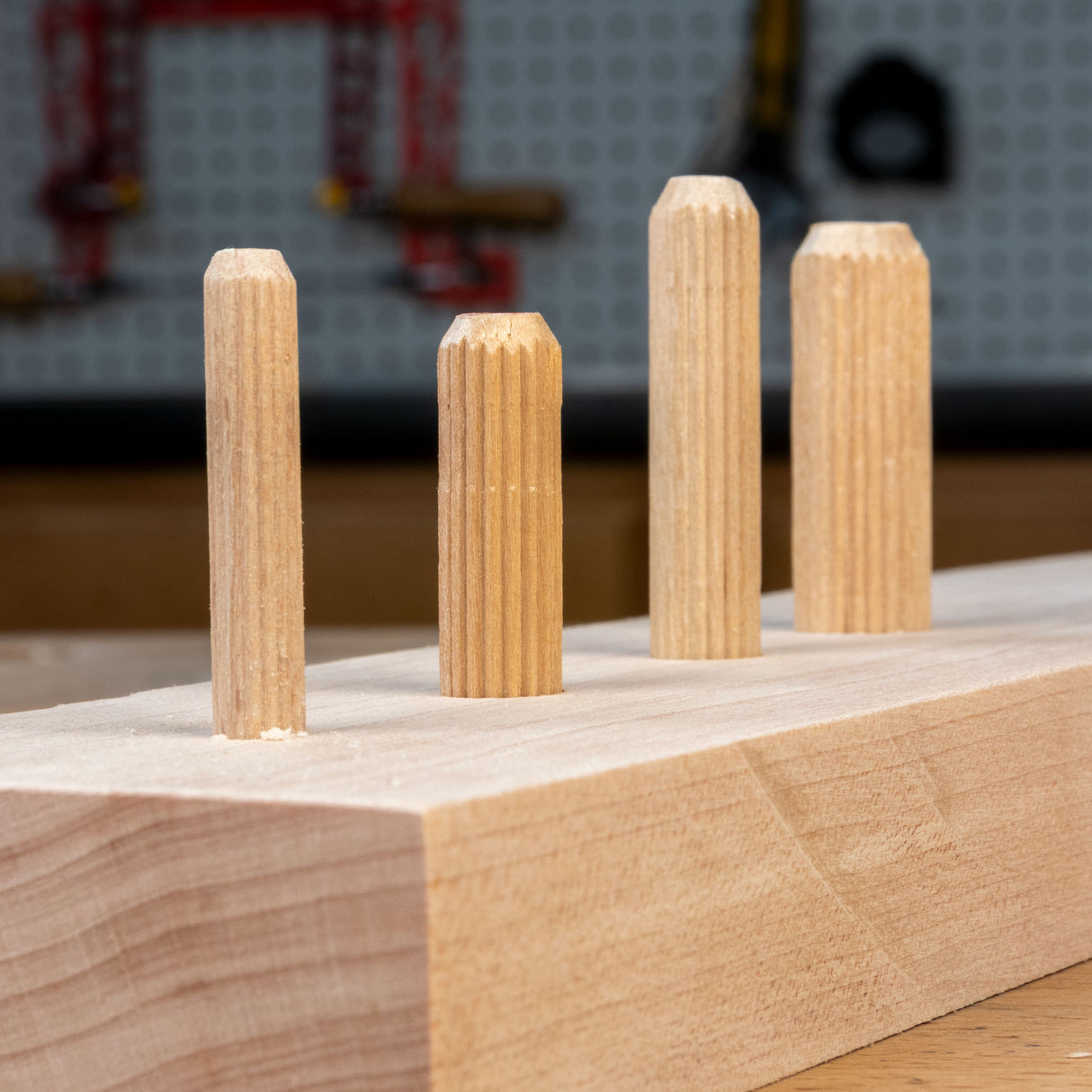 Four wooden dowels on a wooden block with a blurred workshop background