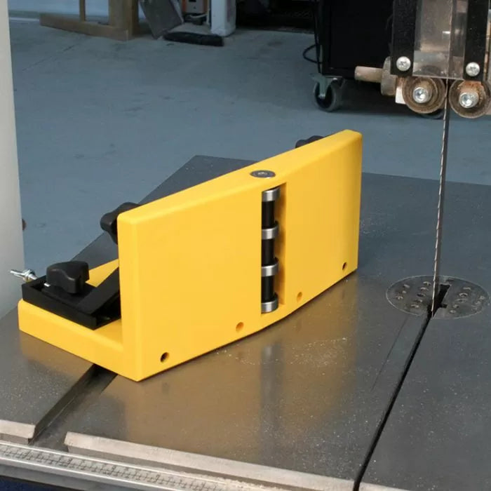 Yellow bandsaw fence jig with roller guides on a bandsaw table in a woodworking shop