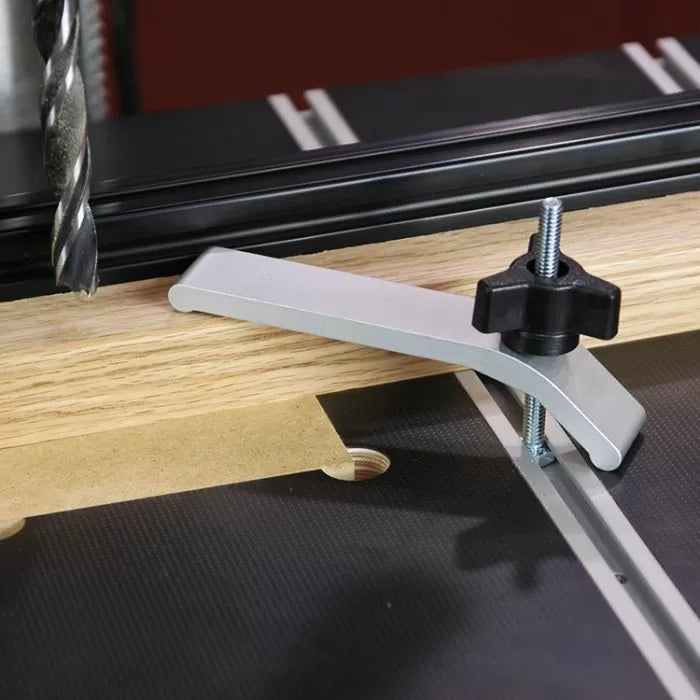 Aluminum hold-down clamp securing wood on a router table with drill bit overhead