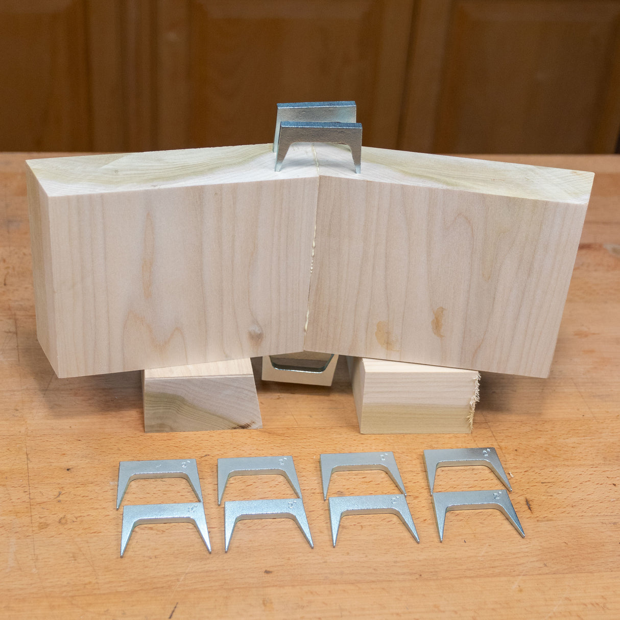 Metal pinch dogs for woodworking displayed with joined wood blocks on a workbench