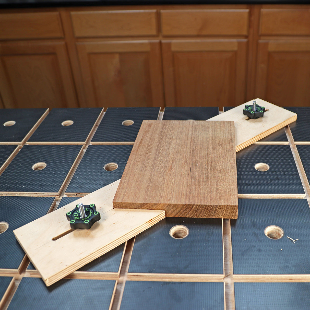 Woodworking jig holding a wood board on a workbench with grid holes in a workshop setting.