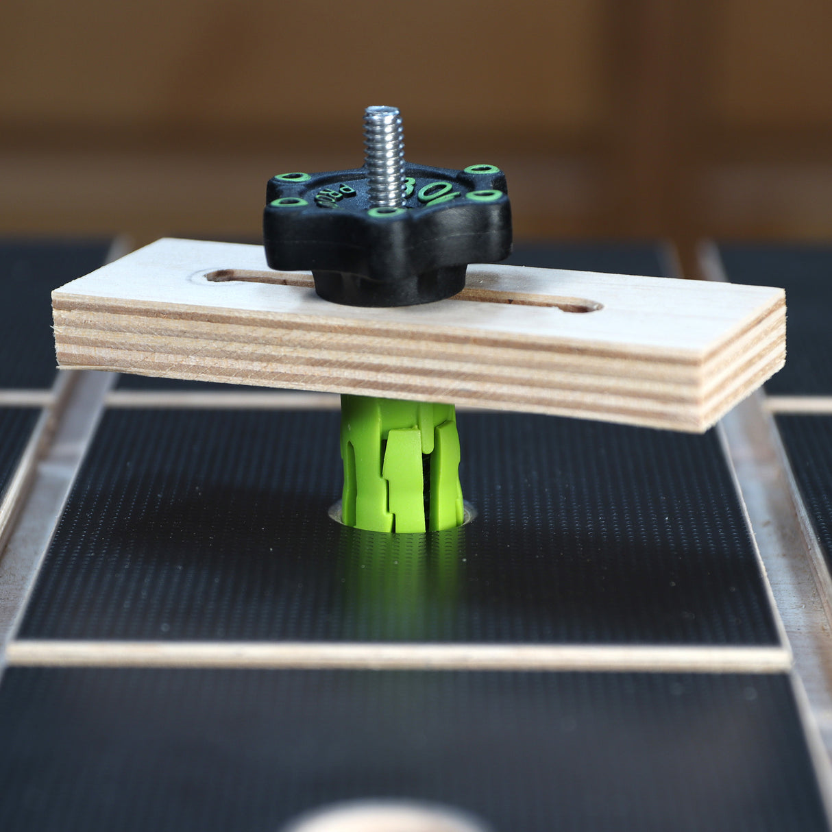 Workbench clamping accessory with green bench dog and plywood hold-down on a textured work surface