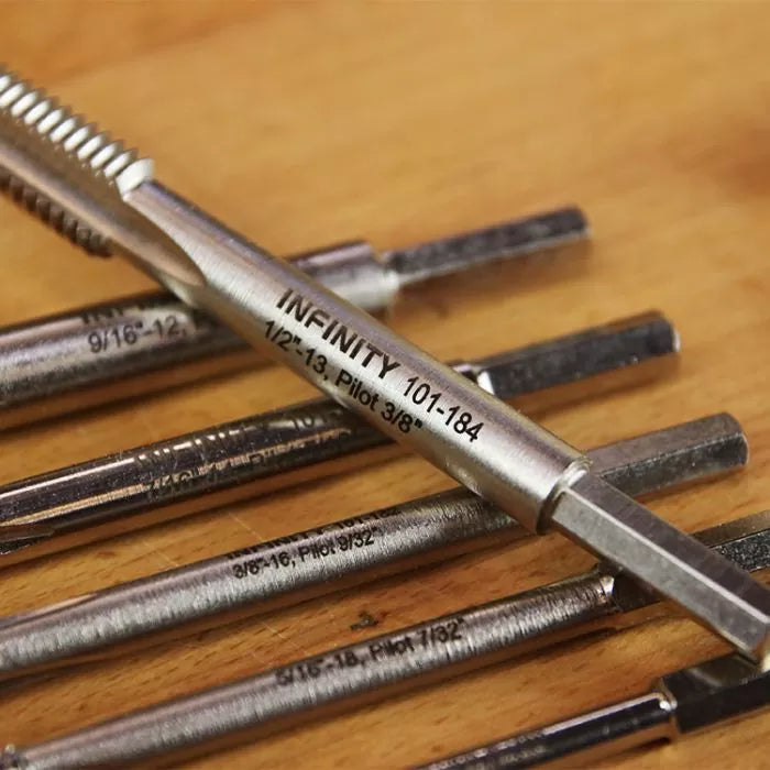 Close-up of metal woodworking plug cutters and thread taps on a wood surface