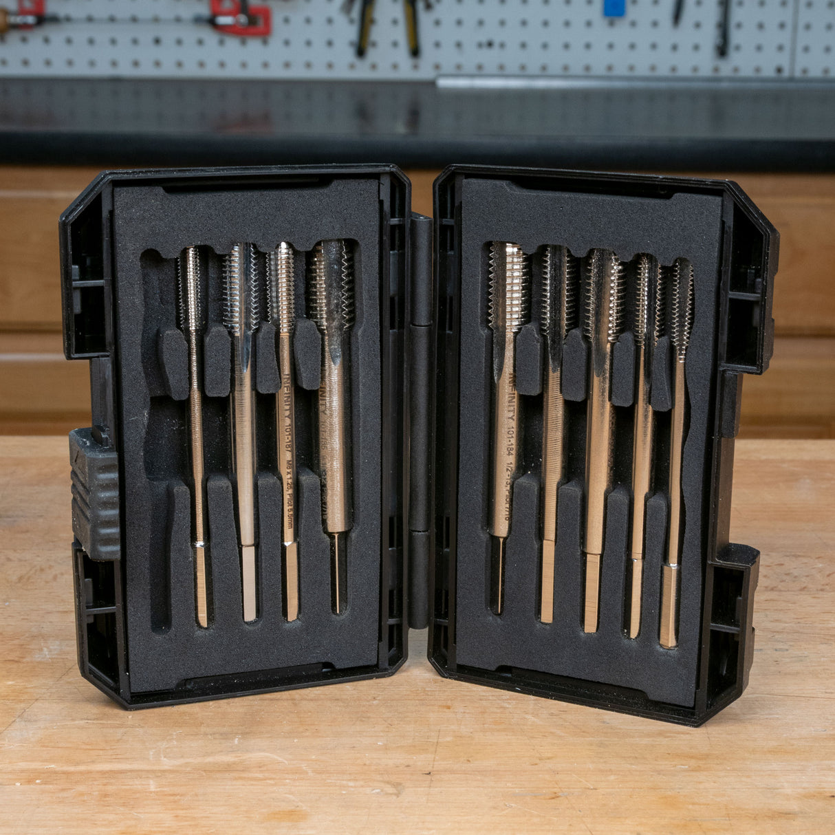 Thread tap set with metal taps in a black protective case on a woodworking bench.