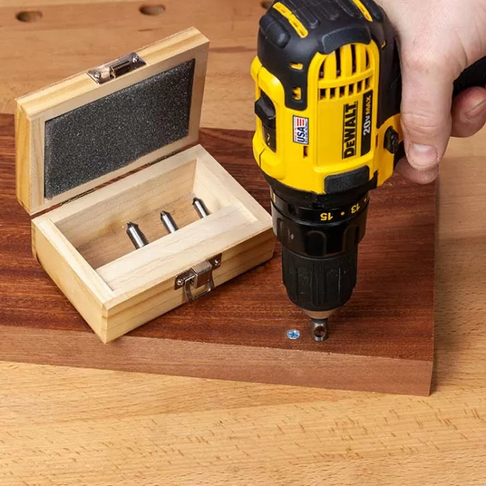 Cordless drill driving screw into wood near a box of woodworking drill bits on workbench