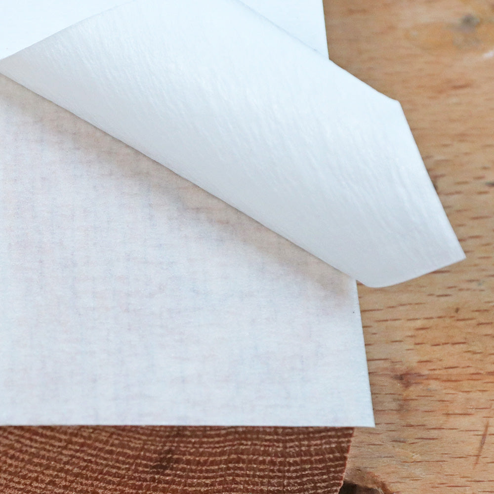 Close-up of adhesive transfer tape being peeled from wood surface on a workbench