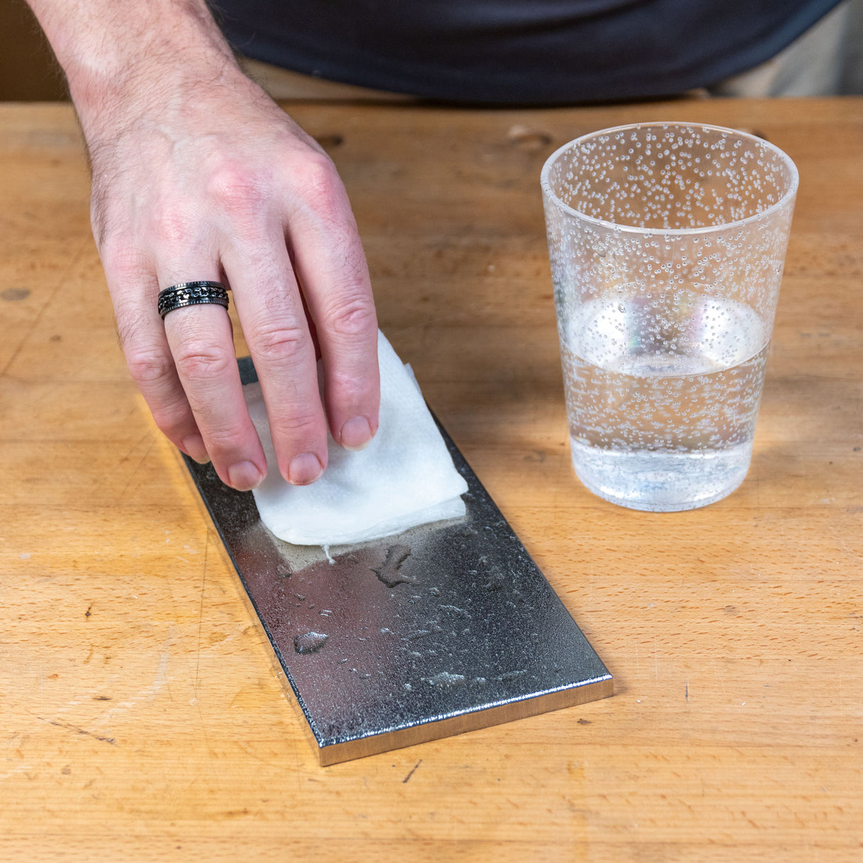 Hand cleaning a steel sharpening plate with a cloth and water on a woodworking bench