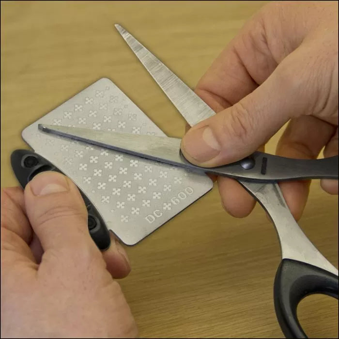 Sharpening scissors blade with diamond sharpening stone on wooden surface