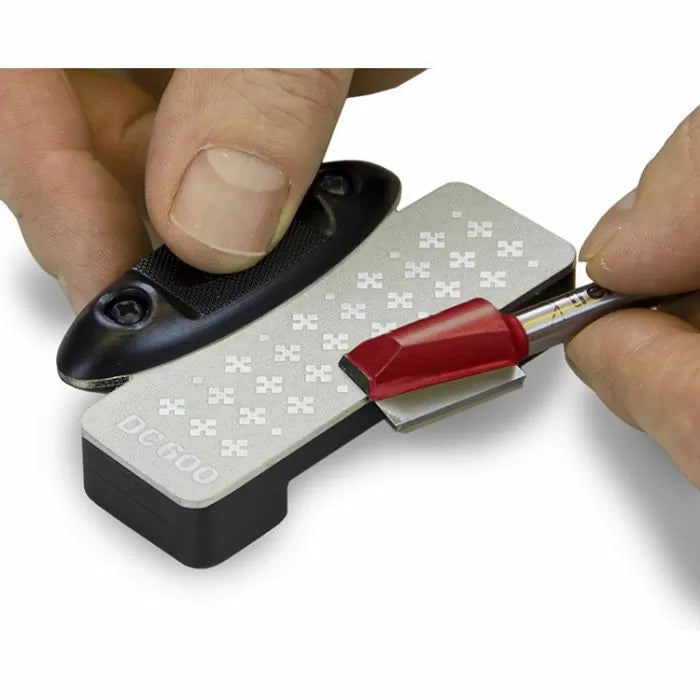 Sharpening a red router bit on a diamond bench stone with hands holding both tools