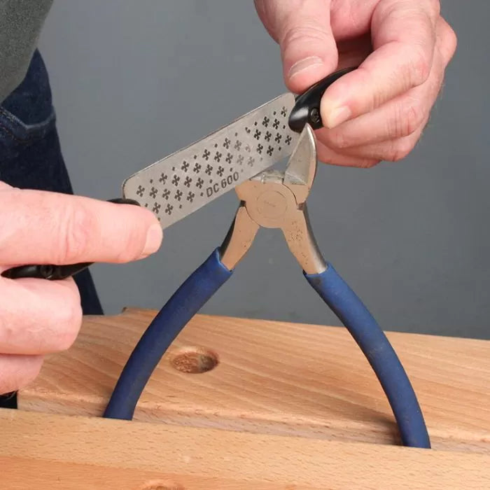 Sharpening wire cutters with a diamond sharpening tool on a wooden workbench