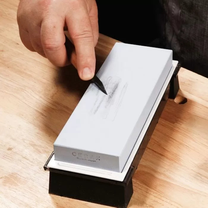Hand drawing on gray sharpening stone on wooden workbench for woodworking tool maintenance