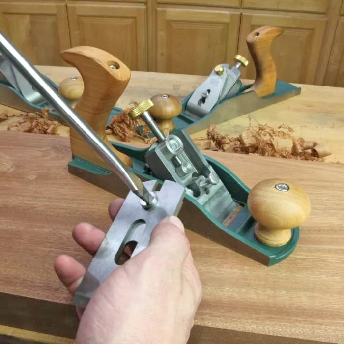 Hand adjusting a metal woodworking hand plane on a workbench with wood shavings