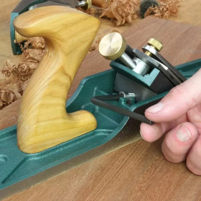 Hand adjusting woodworking hand plane with wooden handle on wood surface