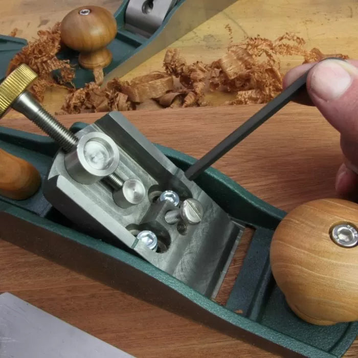 Hand adjusting woodworking hand plane frog screws with hex key on wooden workbench