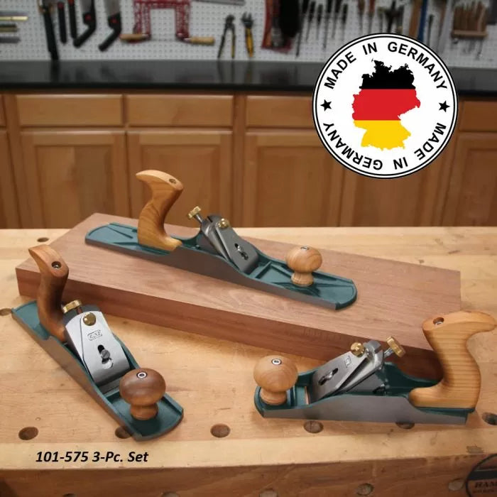 Three German-made woodworking hand planes with wood handles on a workbench in a workshop.