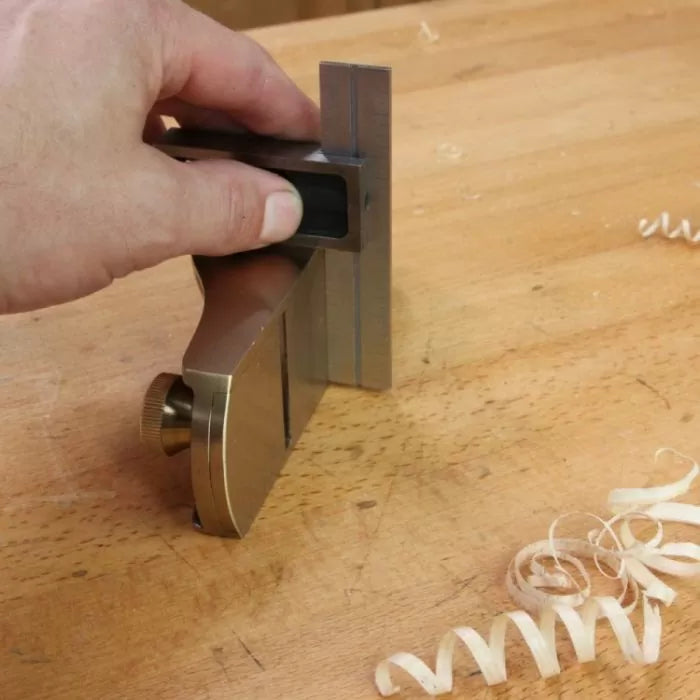 Hand using shoulder plane on wooden workbench with wood shavings, woodworking tool in action