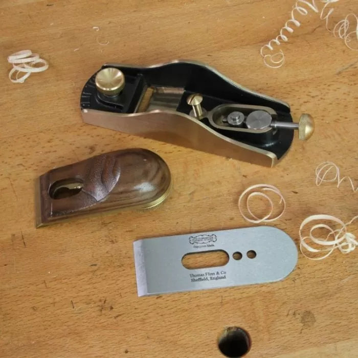 Disassembled hand plane with parts on a woodworking bench, showing blade and cap iron.