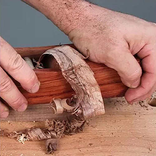 Woodworker using a hand plane tool to smooth a wooden board, creating wood shavings