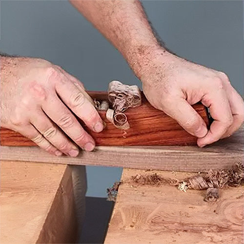 Woodworker using a hand plane tool to smooth wooden board, creating wood shavings