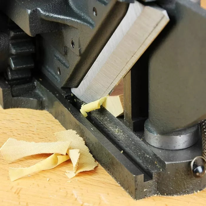 Woodworking miter trimmer cutting wood on a workbench, close-up of sharp blade and wood shavings.