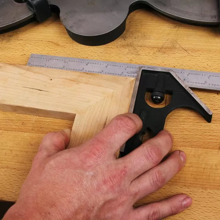 Hand using a combination square to measure a wood miter joint on a workbench