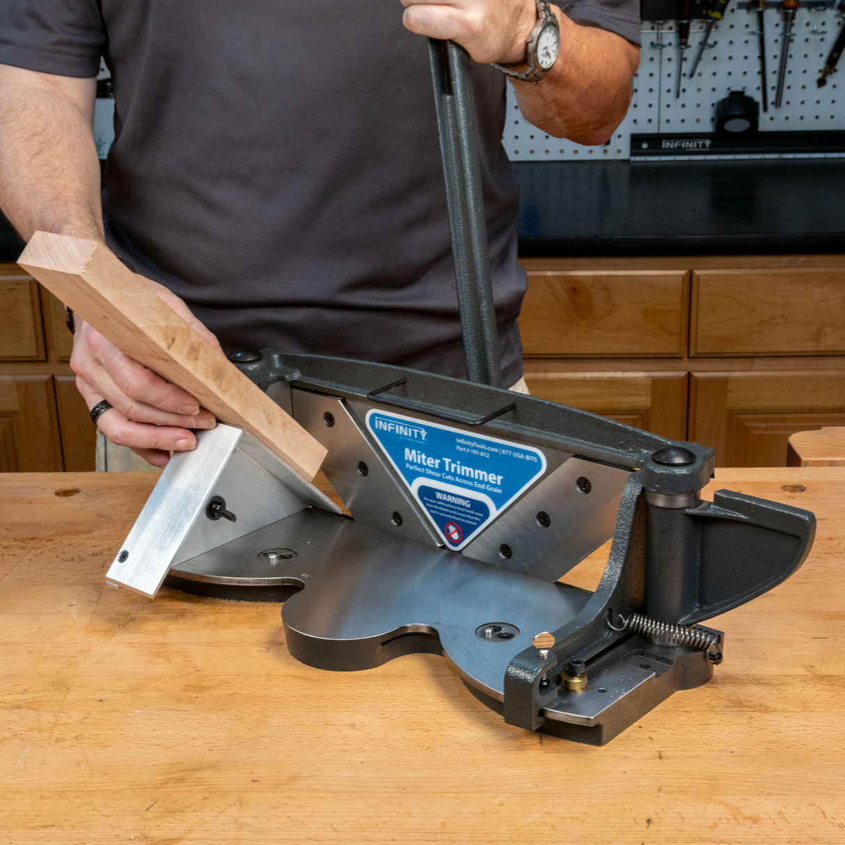 Woodworker using a miter trimmer to cut a precise angle on a wooden board in a workshop.