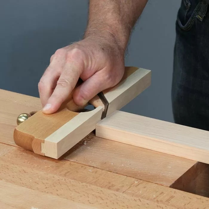 Hand using woodworking shoulder plane to trim tenon on wood bench