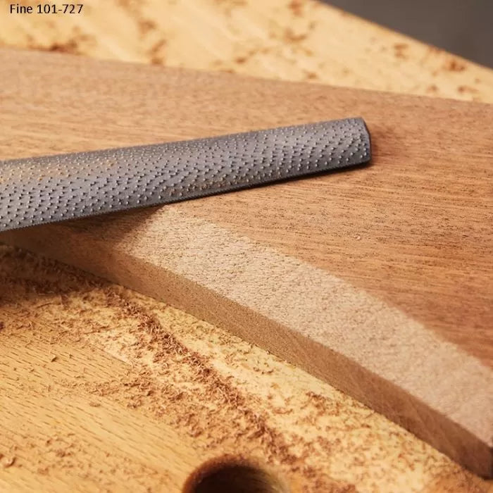 Wood rasp tool smoothing curved wooden edge with fine shavings on workbench