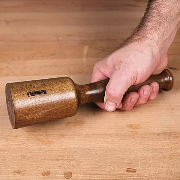 Hand holding wooden woodworking mallet on workbench, ideal for precision joinery tasks