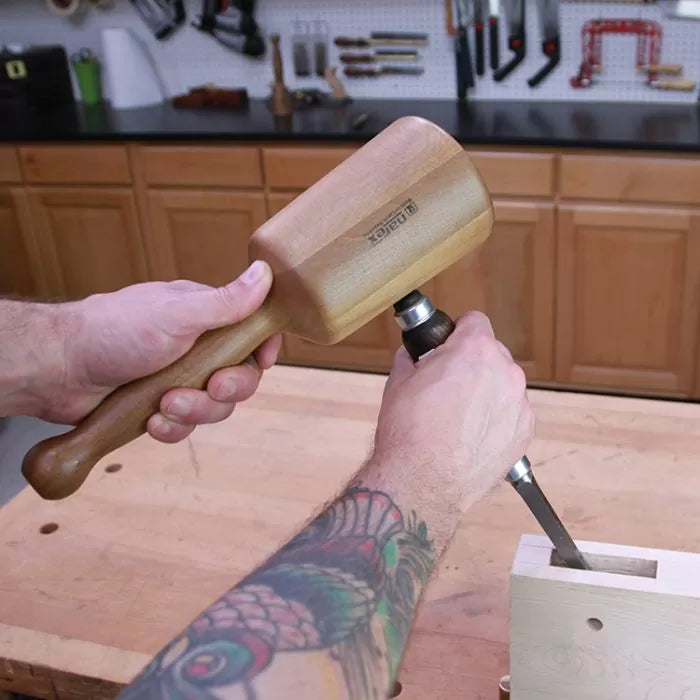 Woodworker using a wooden mallet and chisel on a workbench in a workshop setting