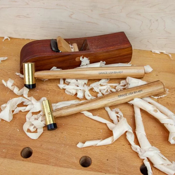 Woodworking bench with two brass head hammers and a hand plane among wood shavings.