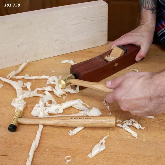 Woodworker using hand plane and brass hammer on wood with wood shavings on workbench