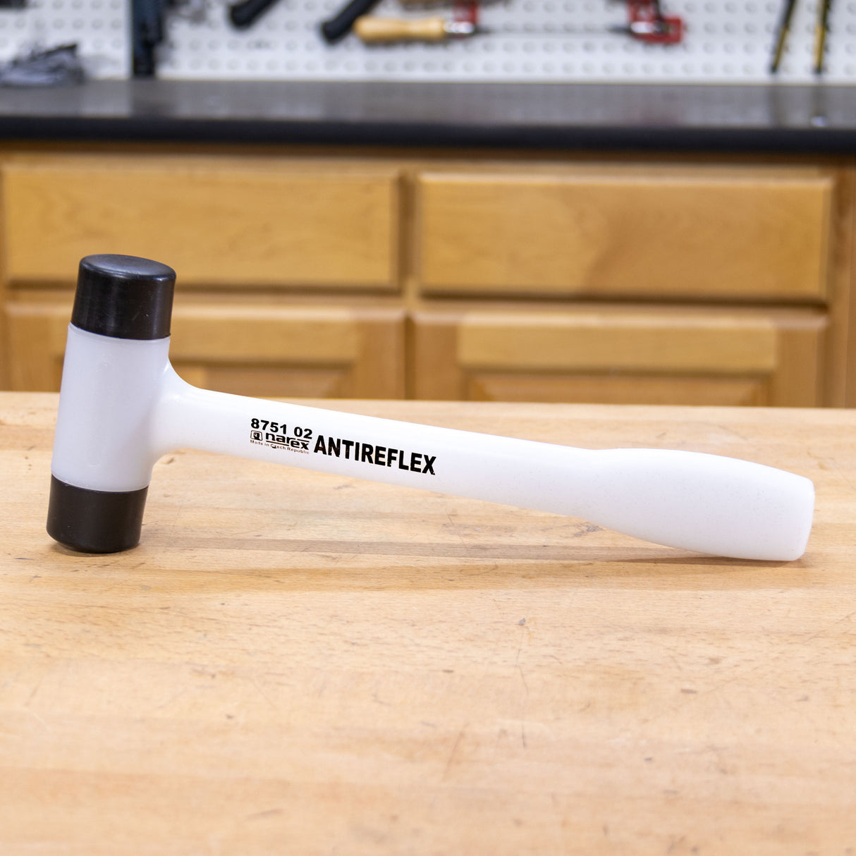 White dead blow mallet with black ends on a woodworking bench in a workshop setting