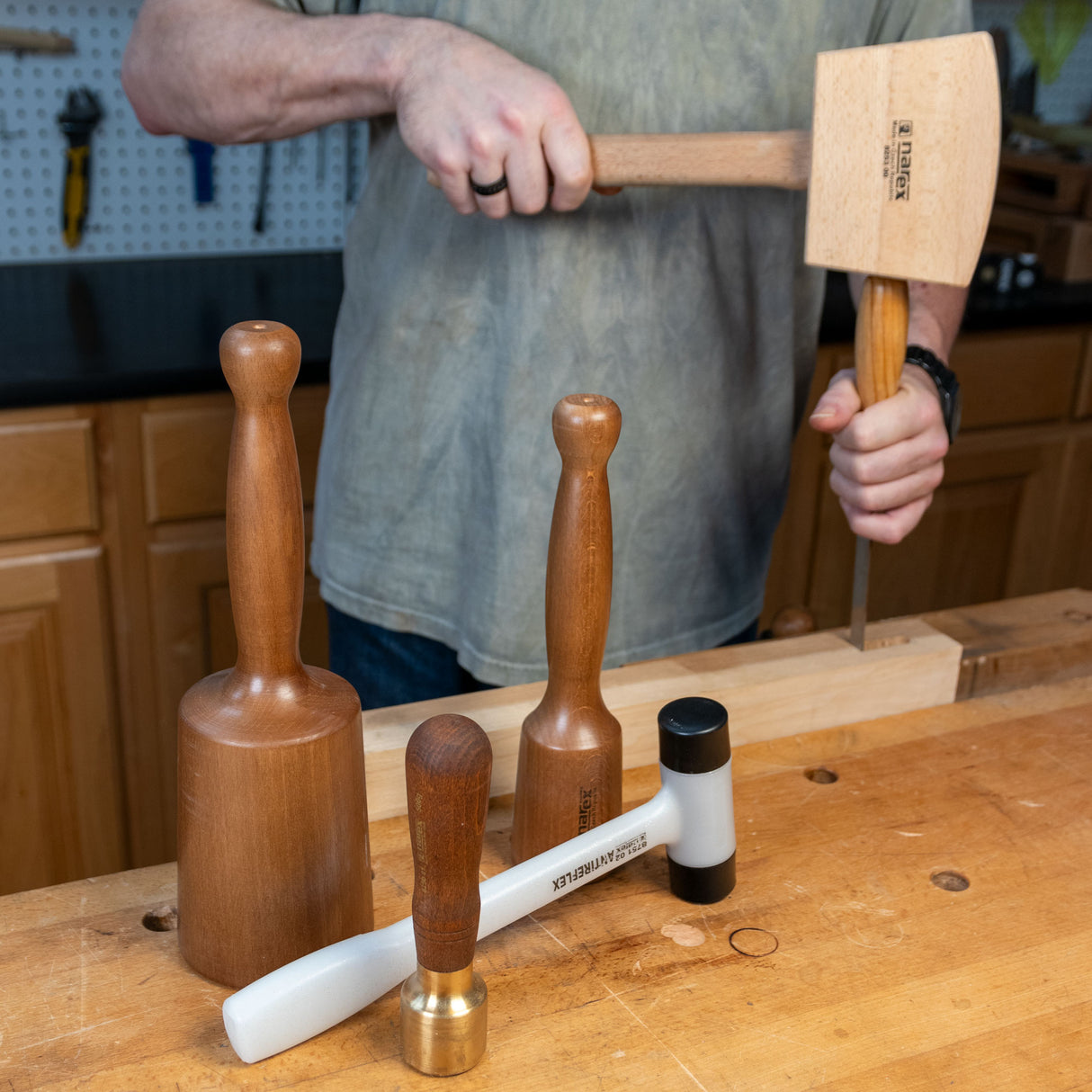 Woodworker using a wooden mallet and chisel at a workbench with various woodworking mallets