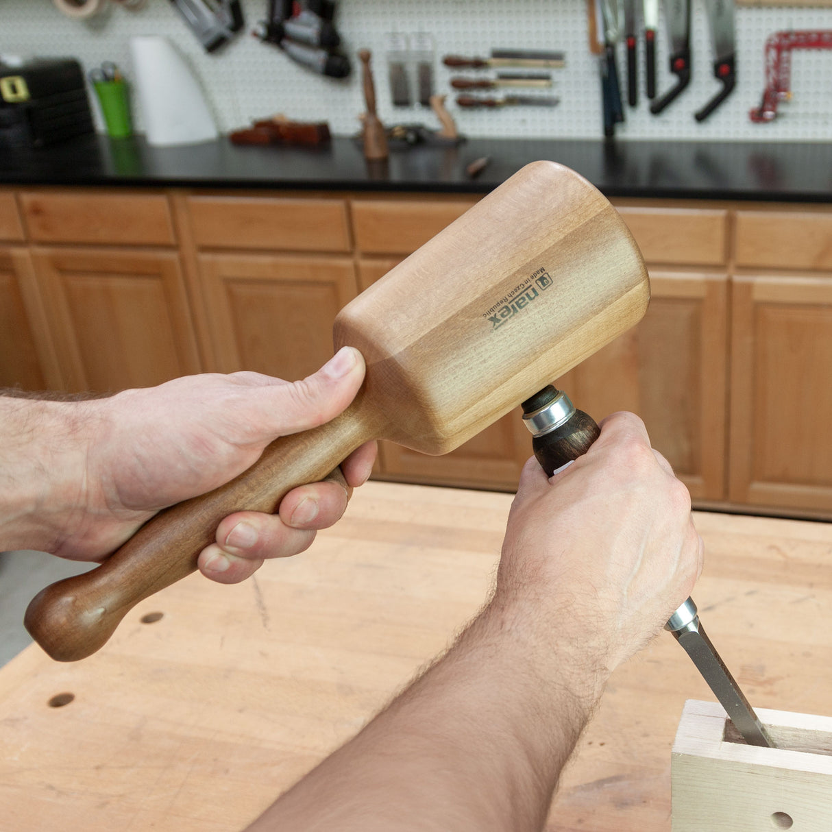 Woodworker using a wooden carver’s mallet and chisel on a workbench in a workshop