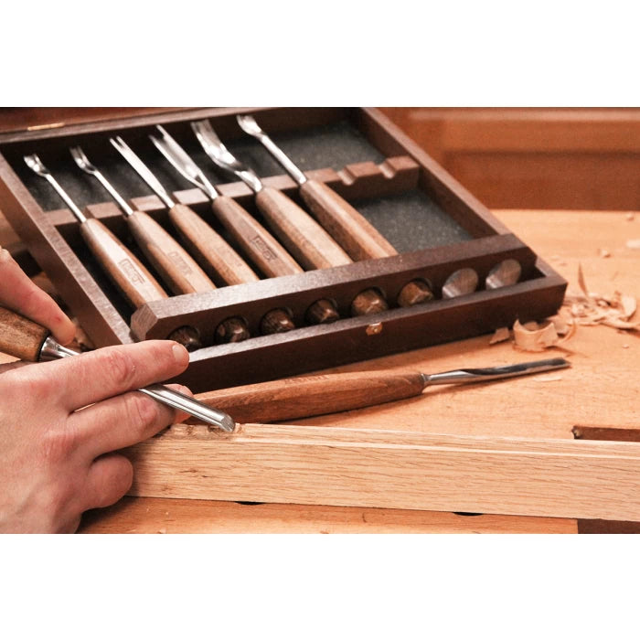 Woodworker using a carving chisel set with wooden handles on a wooden workbench
