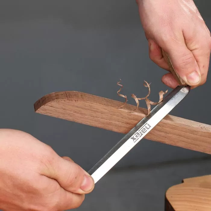 Hand filing wood edge with metal file, creating fine wood shavings, woodworking tools