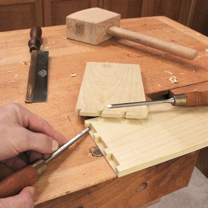 Woodworker using hand chisel and mallet to cut dovetail joints in wooden boards