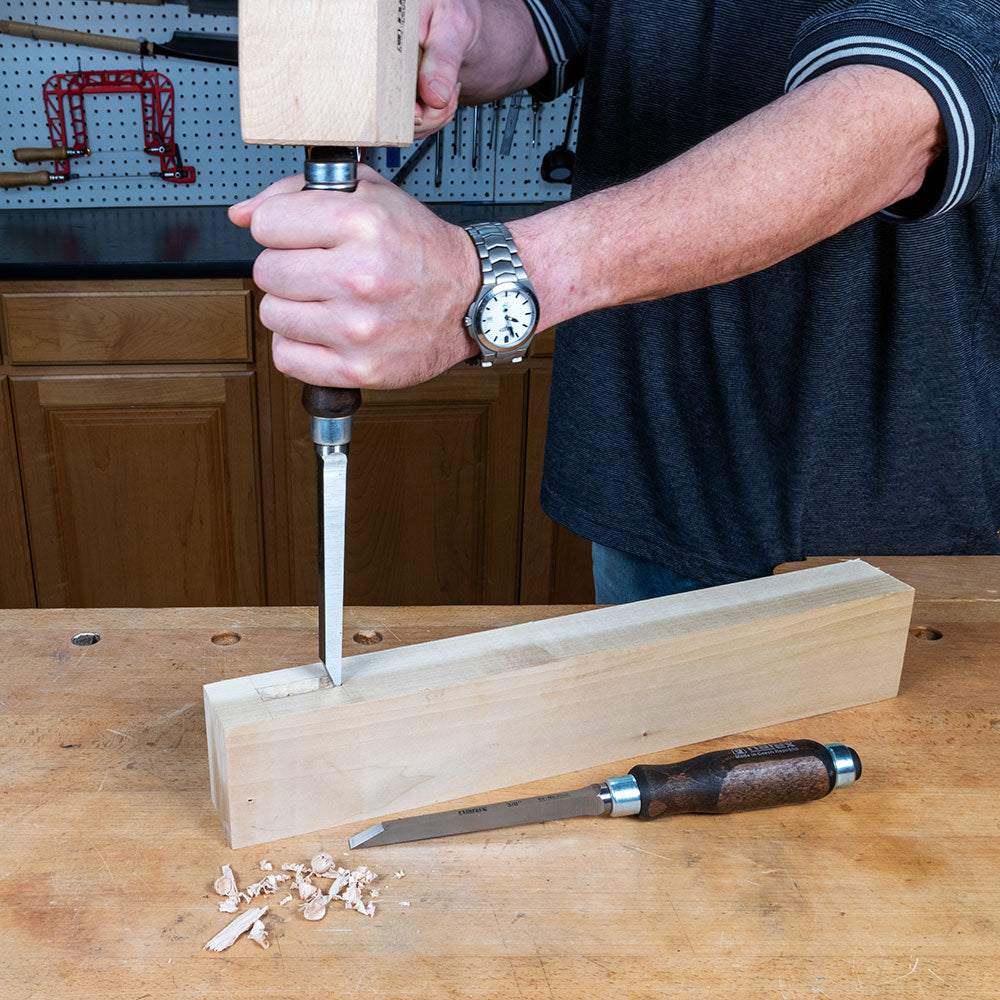 Woodworker using a chisel and mallet to carve a mortise in a wooden beam on a workbench