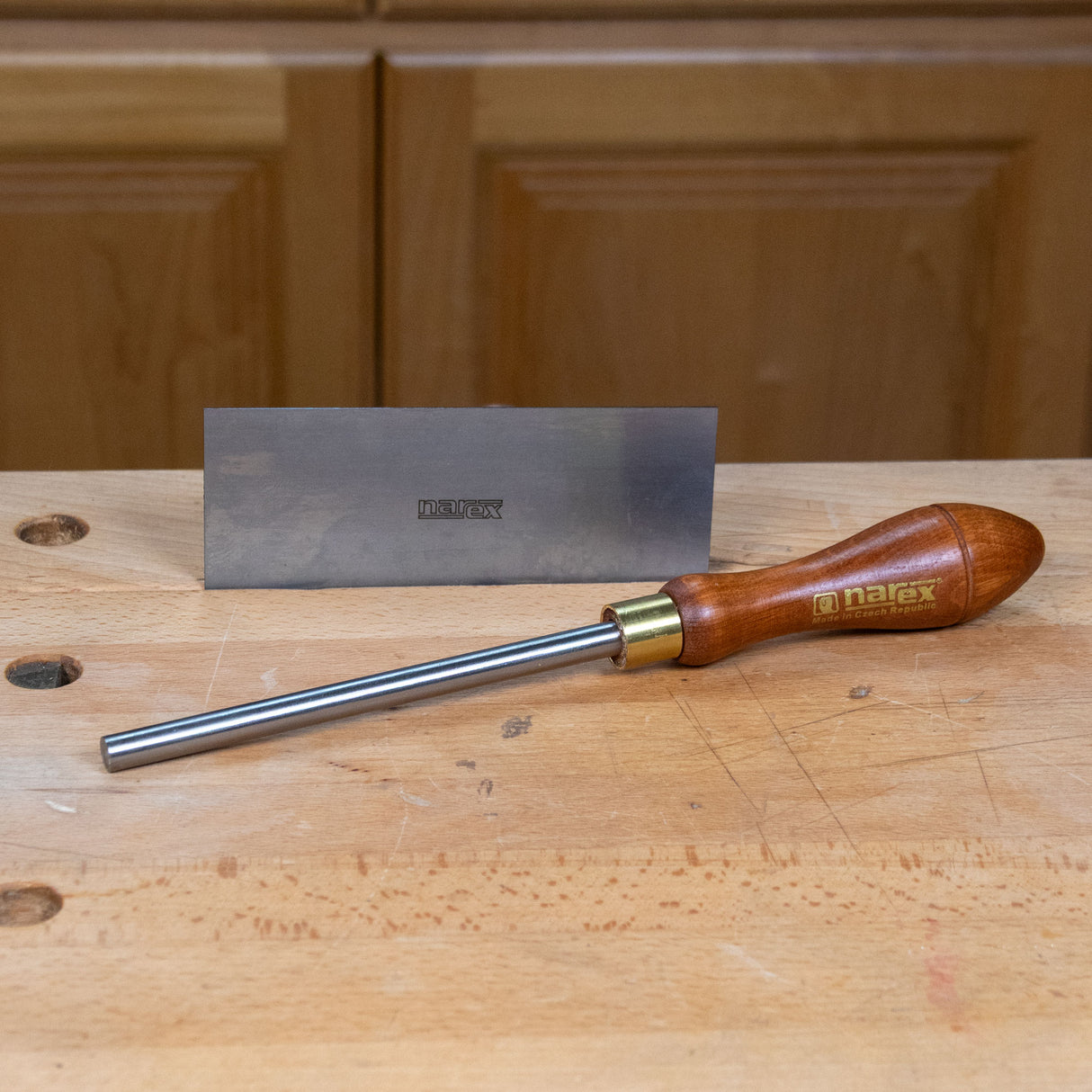 Narex burnisher with wooden handle resting on a workbench beside a sharpening stone