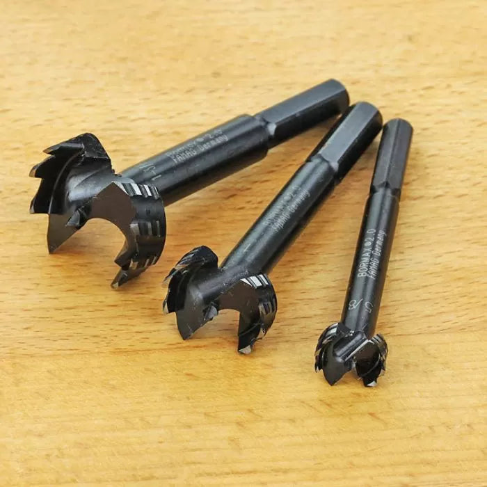 Three Forstner drill bits for woodworking on a light wood surface