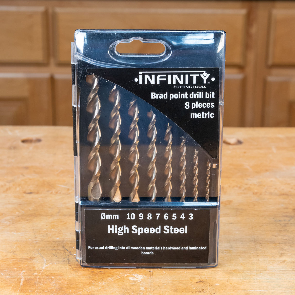 Metric brad point drill bit set, 8 pieces, high speed steel in packaging on wooden workbench.