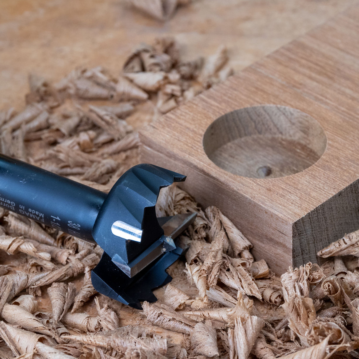Forstner drill bit with wood shavings and bored hole in wooden block on workbench