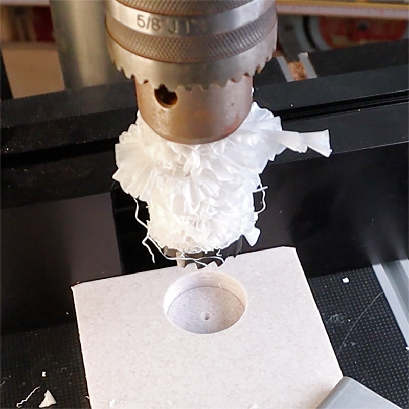 Drill press cutting a precise circular hole in MDF with wood shavings visible