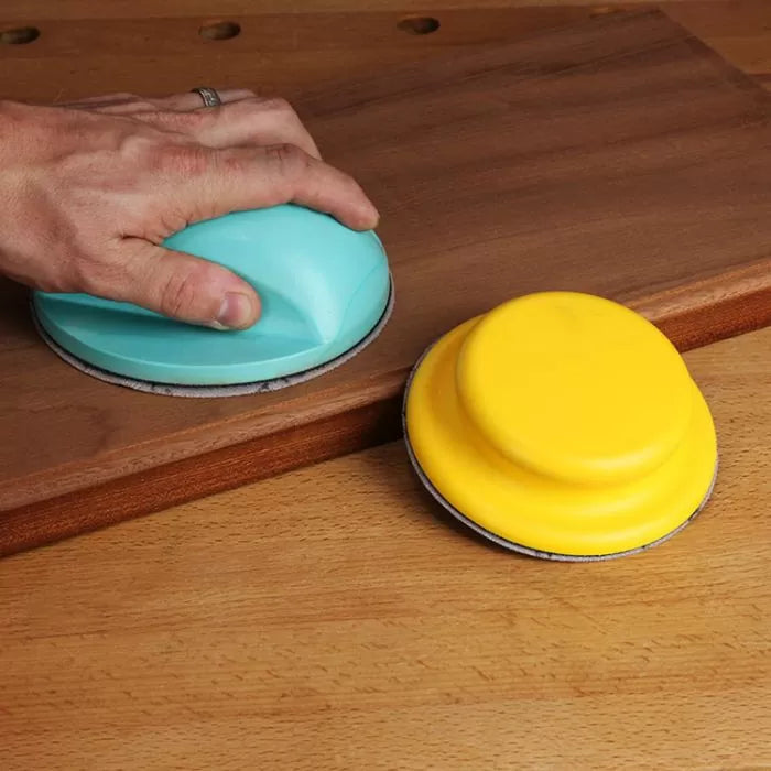 Hand sanding wood with ergonomic sanding disc, second yellow sanding tool nearby