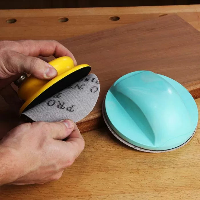 Hand-held sanding blocks with abrasive discs on a wooden surface for woodworking finishing
