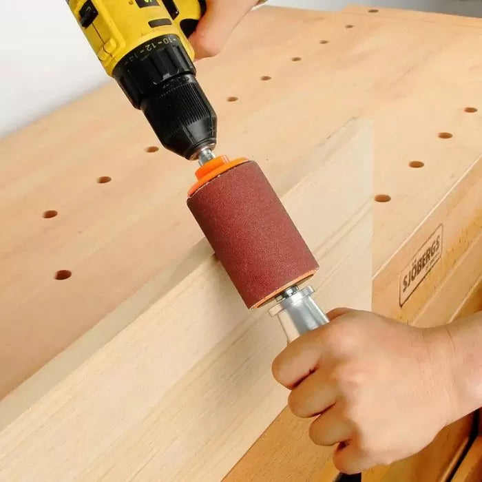 Hand using a drill with sanding drum attachment on wooden board at workbench